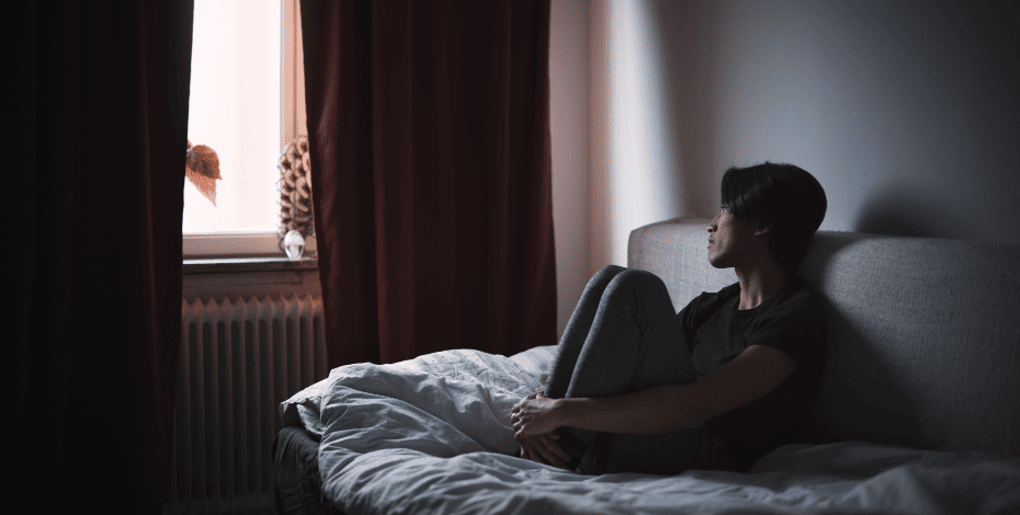A man sitting on his bed, looking despondent 